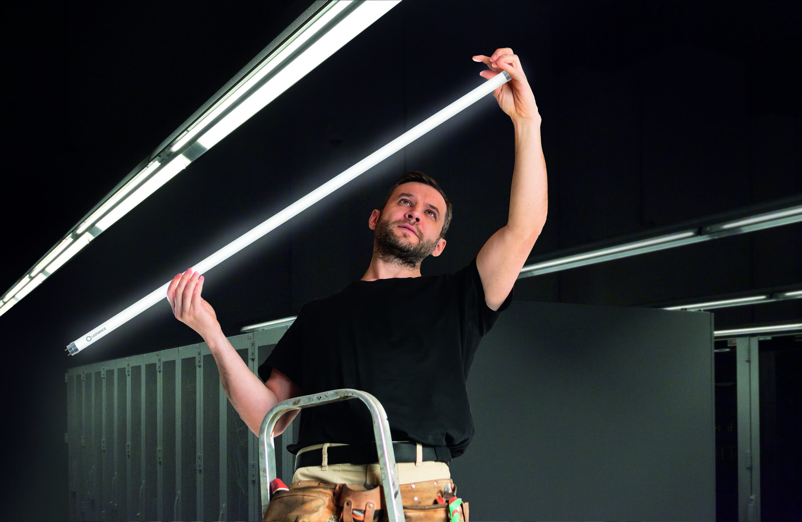 En elektriker kobler lysstoffrør til lamper i et svart tak.